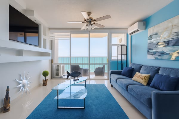 Open-plan kitchen and living room with ocean view through glass doors and white railing on balcony