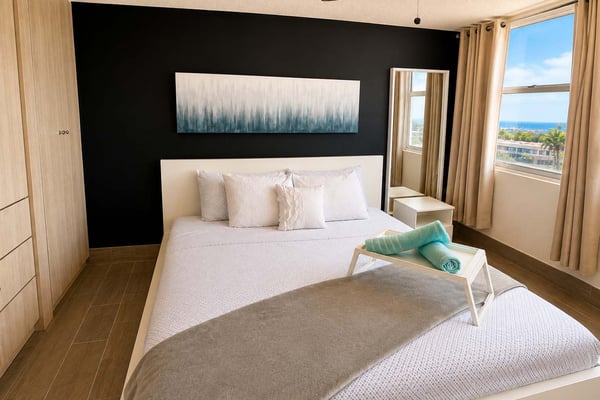 Spacious bedroom with wooden furnishings, two beds, ceiling fan, and open doors leading to a sunny terrace with coastal views