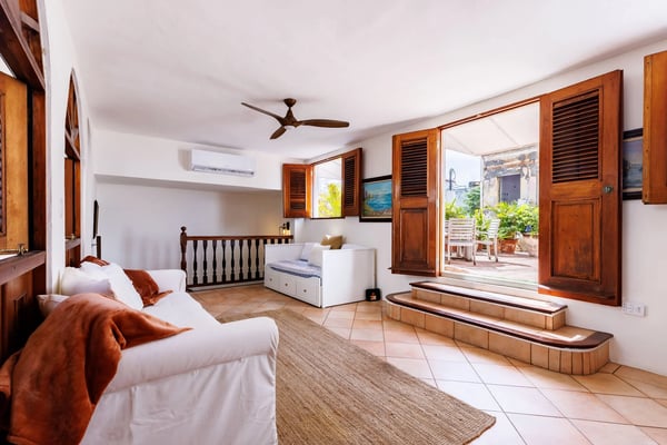Spacious bedroom with two beds, wooden shutters, ceiling fan, and open doors leading to a terrace with sea view