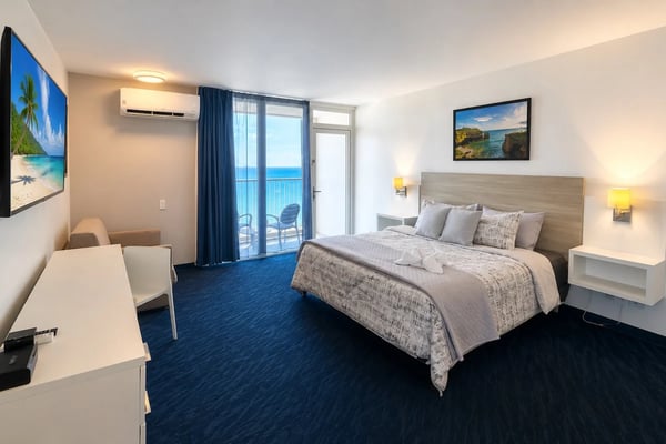 Modern beachfront condo living room with blue sofa, glass coffee table, ocean view balcony, and ceiling fan