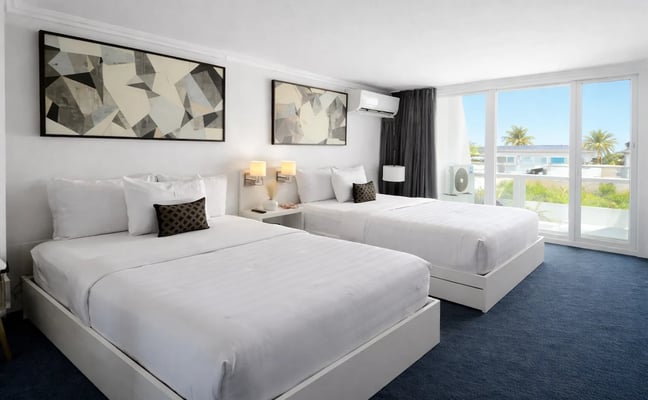 Hotel room with two queen beds, ocean view balcony, blue curtains, and modern furnishings with globe decoration